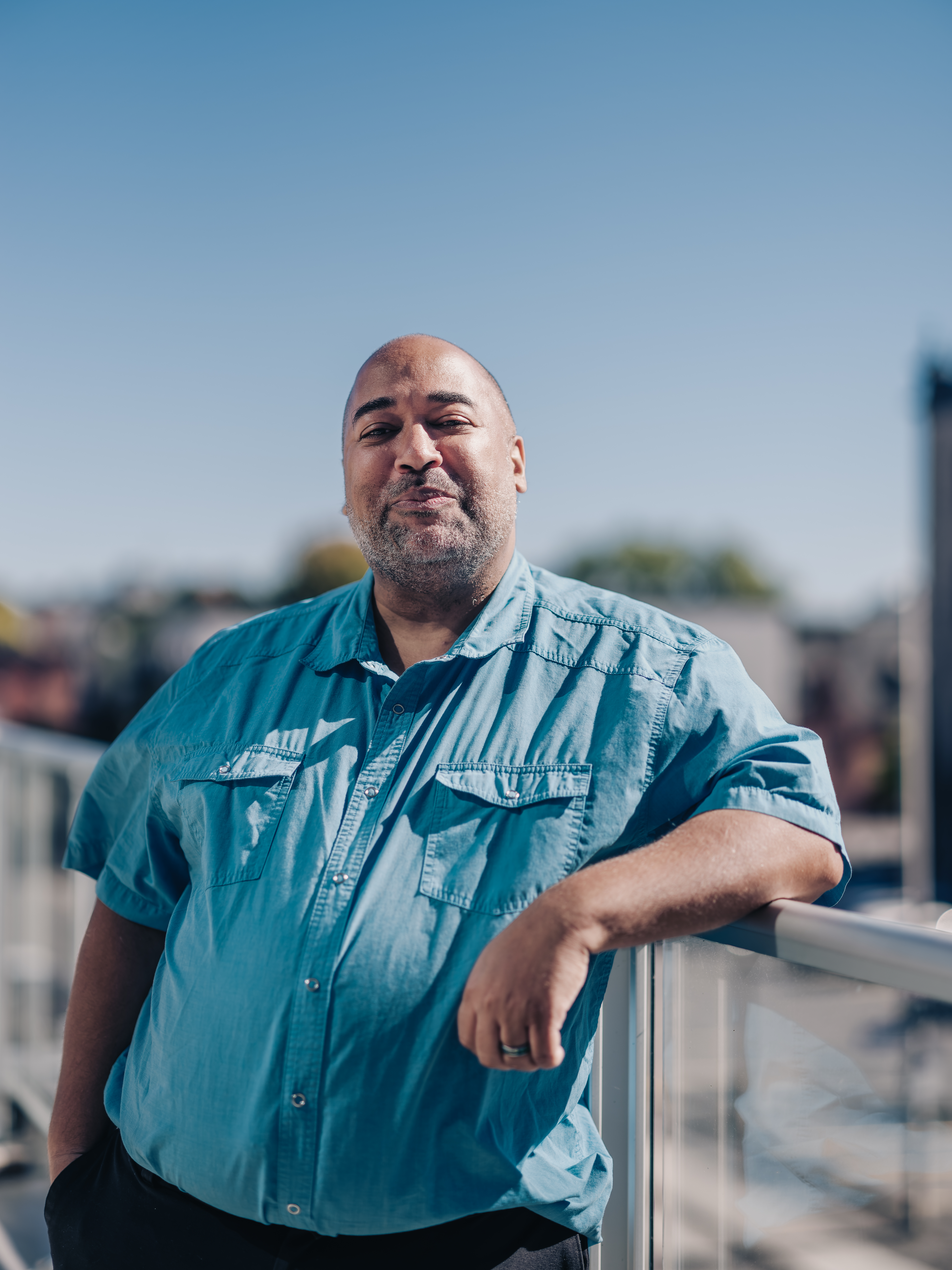 Velvet Wells (Ottawa) stands on the balcony of the Ottawa Art Gallery, the city and skyline blurred behind them. Captured by Curtis Perry Photography (2022)