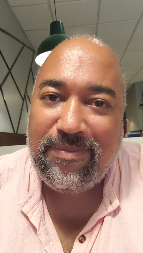 The Velvet Duke is a Black, queer, autistic, disabled, fat person of age, with salt and pepper beard and wearing a salmon shirt. They love the lighting of this restaurant selfie